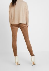 Suéter de punto beige con un ajuste relajado, combinado con pantalones ajustados de imitación ante marrones y botas blancas de tobillo con tacones altos.
