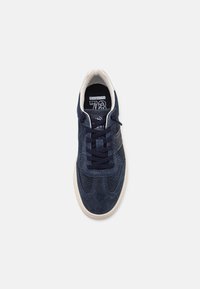 Tengerészkék velúr sneaker perforált kialakítással, bézs gumitalppal és sötét cipőfűzőkkel. Az orrán márkajelzés található.