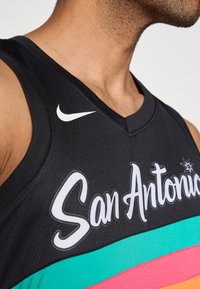 Tricou de baschet negru cu inscripția „San Antonio” în alb, cu dungi orizontale turcoaz, roz și negru și un logo Nike pe umăr.