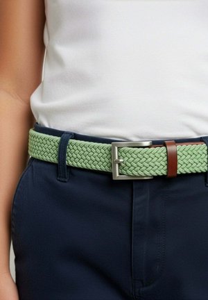 Gros plan d'une personne portant un pantalon bleu marine et une ceinture tissée vert clair avec une boucle rectangulaire argentée et une boucle en cuir marron.