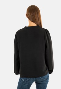 Maglione nero con maniche a sbuffo, scollatura arrotondata e tessuto testurizzato. Indossato con jeans blu, che mostrano un look casual.