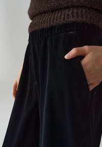 Zwarte fluwelen wijde broek met een elastische tailleband en zijzakken, met een zachte textuur en een ontspannen pasvorm.