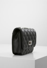 Czarna skórzana torebka crossbody o pikowanym wzorze, z metalowymi elementami w kolorze srebra i z klapką na zamek. Posiada łańcuszkowy pasek, co zapewnia wszechstronność noszenia.