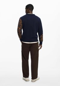 Navy sweater with orange paisley patterned sleeves, ribbed cuffs and hem, paired with brown cargo pants and white sneakers.