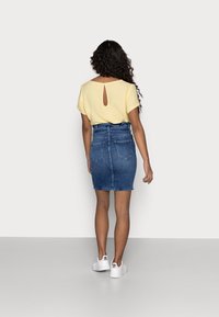 Gul topp med nyckelhålsöppning bak, i kombination med en högmidjad denimkjol som har en figurnära passform och två bakfickor. Vita sneakers fulländar looken.