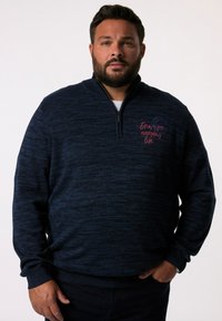 Marinblå zip-up tröja med texturerad yta. Har broderad text i röd, ståkrage samt ribbad ärm och nederkant.