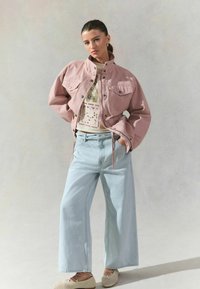 Veste en denim rose avec un col et des poches avant, associée à un jean large bleu clair et des slip-ons tissés beige.