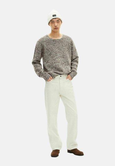 Maglione a maglia marrone e bianco a pois, pantaloni dritti crema e stivali in suede marrone, il tutto completato da un cappello di lana bianco.