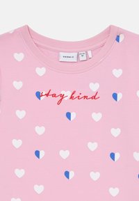 Felpa rosa chiaro con motivi a forma di cuore bianchi e blu, con la frase "stay kind" ricamata in rosso al centro.