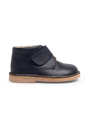 Bota de cuero negro para tobillo con una correa de Velcro, punta redondeada y suela de goma color beige. Presenta costuras a lo largo de la suela para un detalle adicional.