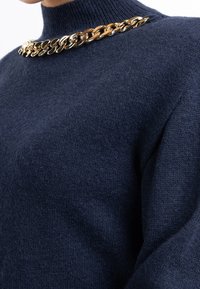 Tmavě modrý pletený svetr s vysokým límcem a ozdobným zlatým řetízkem na lícovém lemu. Měkká textura, uvolněný střih a bez viditelných vzorů.
