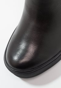 Pointe de botte en cuir noir avec une surface lisse, légèrement texturée, et une semelle noire épaisse sur fond blanc.