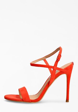 Sandale à talon haut en daim orange avec une fine bride de cheville, bout ouvert et talon aiguille. Le design présente des détails entrecroisés et une texture lisse.