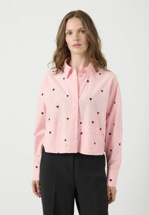 Chemise rose courte avec motifs de cœurs noirs, boutonnière devant, col et deux poches avant ; associée à un pantalon noir en coton fin.