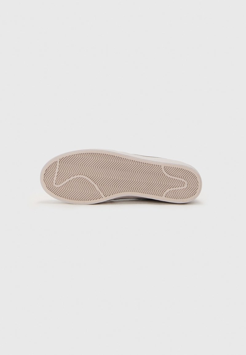 Suola della scarpa con un motivo a spina di pesce, realizzata in gomma. Il colore è beige con una superficie liscia e leggermente texture.