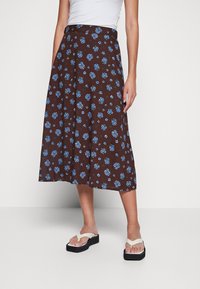 Falda midi marrón con flores azules, diseño en línea A, tejido ligero, combinada con chanclas blancas con plataforma negra.