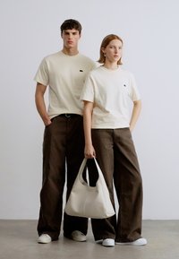 Μπεζ βαμβακερά t-shirts με μικρό λογότυπο, άνετο καφέ παντελόνι, λευκά αθλητικά παπούτσια και μια ώχρας τσάντα ώμου. Απλός, καθημερινός σχεδιασμός.