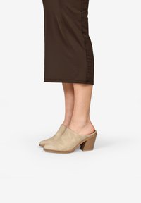 Mules de ante beige con puntera redondeada y parte trasera abierta, que cuentan con un tacón bloque texturizado y una superficie suave.