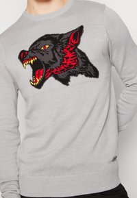 Pull en maille grise avec un grand motif de panthère noire et rouge rugissante sur le devant. Encolure ronde et coupe ajustée aux poignets et à l'ourlet.