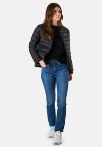 Giubbotto imbottito nero con texture a quadri, indossato sopra una maglietta nera, abbinato a jeans blu e sneakers bianche. Design semplice e funzionale.