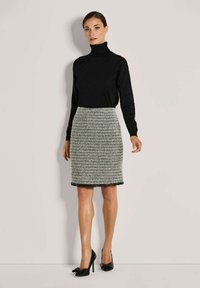 Schwarzer Rollkragenpullover kombiniert mit einem strukturierten, mehrfarbigen Tweedrock mit Fransenabschluss. Getragen mit schwarzen High Heels.