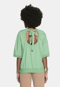 Zielony bawełniany top o szerokim kroju, krótkich rękawach, z zapięciem na wstążkę z tyłu oraz okrągłym wycięciem. Miękka tekstura i luźny krój.