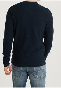 Granatowy sweter z długim rękawem o teksturowanym splocie, z okrągłym dekoltem i dopasowanym wykończeniem, w połączeniu z jasnoniebieskimi dżinsami.
