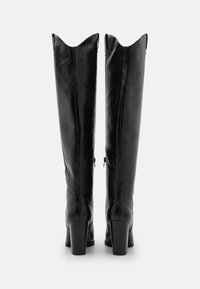 Botas de cuero negro hasta la rodilla con un corte en punta, tacones cuadrados y una textura suave, que cuentan con cremalleras laterales para facilitar su uso.