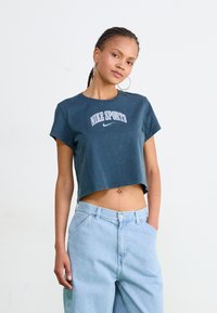 Cropped navy t-shirt with short sleeves and white "NIKE SPORTS" print; paired with light denim wide-leg jeans. Smooth cotton texture.