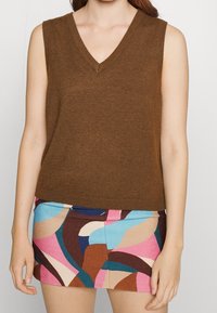 Haut marron sans manches à col en V avec un ourlet côtelé, associé à une mini-jupe à motifs multicolores présentant des tourbillons de rose, bleu et marron.