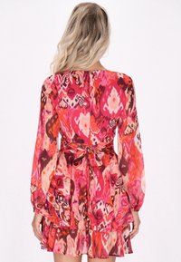 Rochie cu imprimeu floral în nuanțe de roz, roșu și portocaliu. Are mâneci lungi, talie fitted cu un accent legat și o margine volanată.