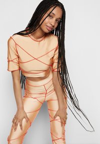 Conjunto ajustado de duas peças em tecido brilhante de pêssego, com costuras laranja em destaque. Top curto com mangas curtas e leggings de cintura alta.