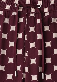 Tissu à motif géométrique bordeaux et blanc avec taille élastique et cordons bordeaux munis d'embouts métalliques argentés.