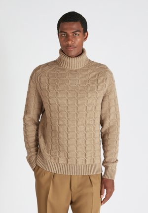 Suéter de tortuga beige de punto con un patrón geométrico texturizado, puños y dobladillo acanalados; combinado con pantalones color tierra.