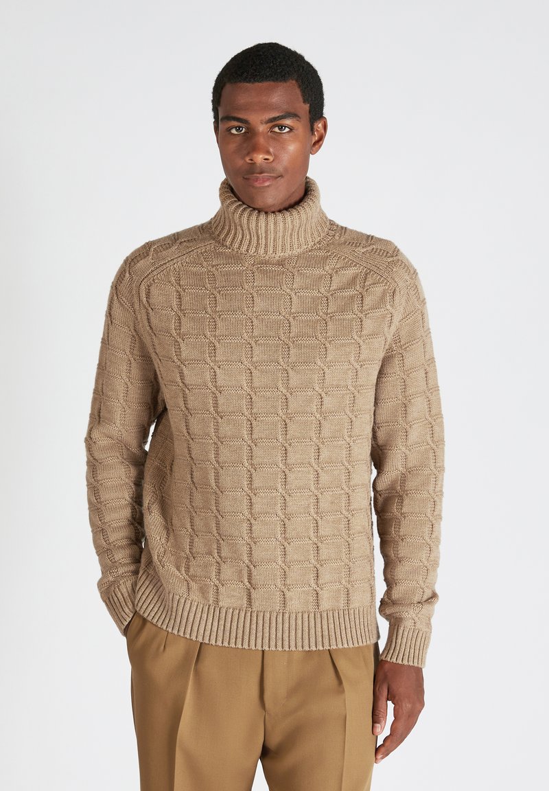Pullover beige a collo alto lavorato a maglia con un motivo geometrico testurizzato, polsini e orlo a costine; abbinato a pantaloni color cammello.