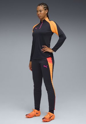 Ensemble de vêtements de sport comprenant un haut noir à manches longues avec des accents orange, un pantalon noir assorti avec des rayures latérales orange et des baskets orange.