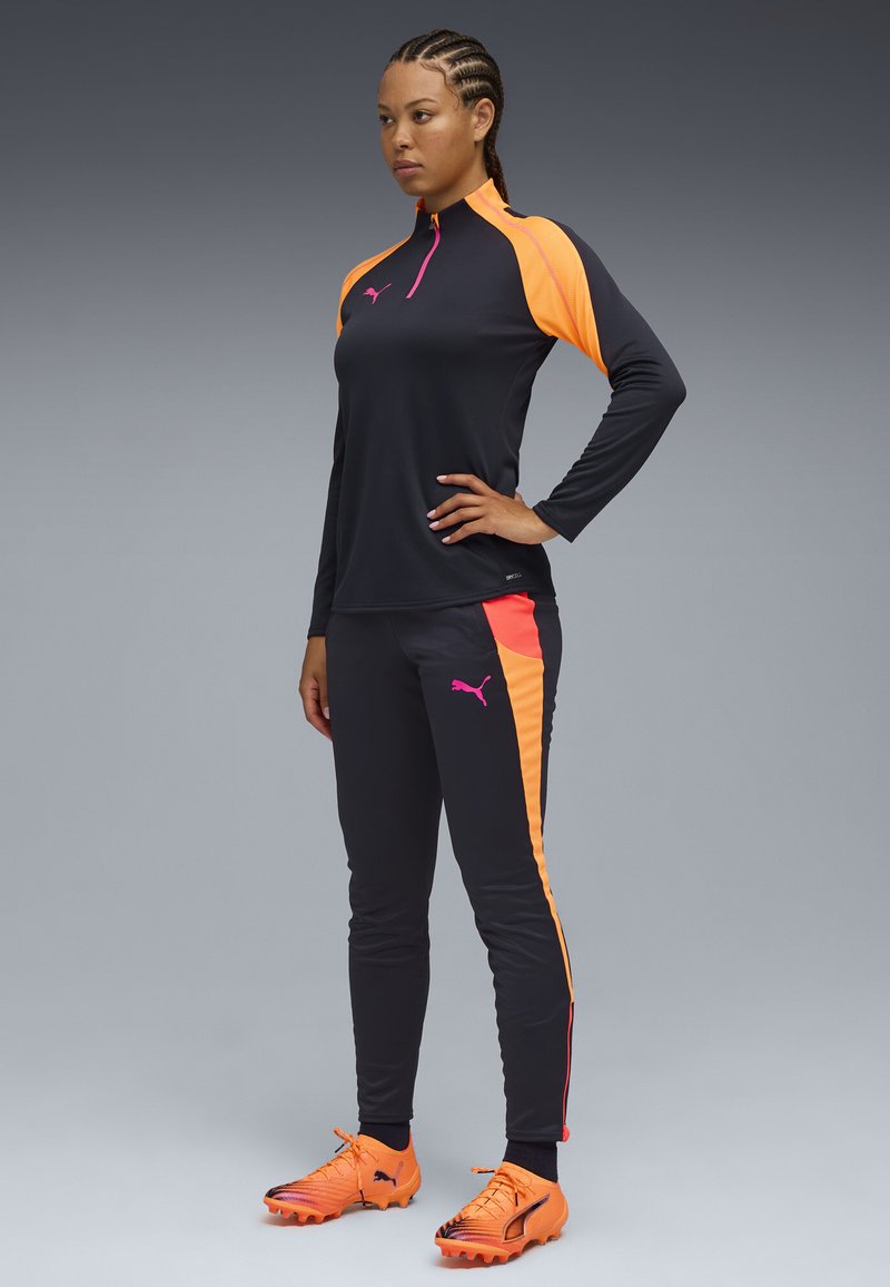 Completo sportivo composto da un top a maniche lunghe nero con dettagli arancioni, pantaloni neri abbinati con strisce laterali arancioni e scarpe arancioni.