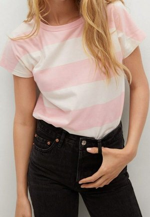 Kvinde iført en pink og hvid stribet kortærmet skjorte, der er stoppet ned i et par højtsiddende sorte jeans, som holder ved fronten af linningen.
