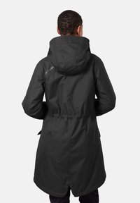 Svart vattentät jacka med huva, åtdragen midja och lång passform, med en lätt kurva på fållen och logotypdetalj på axeln.