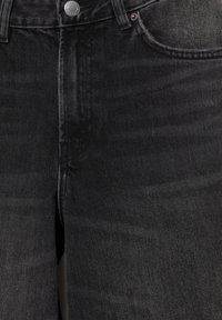 Czarne dżinsy z denimu, zbliżenie na guzik, zamek błyskawiczny, szlufki na pasek oraz przednie kieszenie z detalami z miedzianymi nitami.