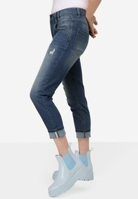 Tummansinisiä, keskiharmaiden farkkujen, joissa on käänteet ja repäisydet. Yhdistetty vaaleansinisiin liukuhihnakenkiin.