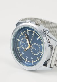 Silver and blue chronograph watch with a mesh strap, featuring a dark blue dial, gold accents, and two sub-dials for timing.