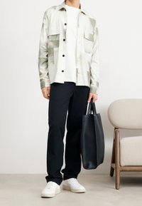 Camisa de cuadros en tonos claros, camiseta blanca, pantalones negros, zapatillas blancas, bolsa de mano negra. Diseño minimalista con bolsillos funcionales.