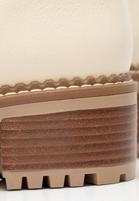 Primer plano del tacón de un zapato de cuero beige con suela de madera apilada marrón y suela de goma estriada.