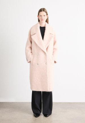 Cappotto doppiopetto in morbido tessuto rosa chiaro, dotato di ampio colletto, bottoni argento e tasche laterali, abbinato a pantaloni neri a gamba larga.