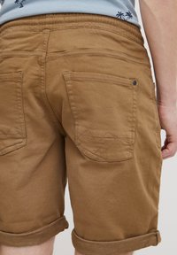 Pantaloni scurți maro din bumbac, cu tiv răsucit, buzunare în spate cu cusături diagonale și talie elastică pentru confort.