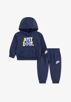 Tamsiai mėlynos spalvos medvilnės džemperis ir kelnės. Džemperis turi geltoną, mėlyną ir baltą užrašą "JUST DO IT."; kelnėse – Nike logo.