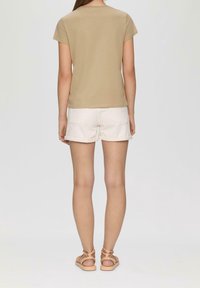 Beige cotton t-shirt with short sleeves, paired with white denim shorts. Sandals with crisscross straps and flat soles. Simple and casual design.