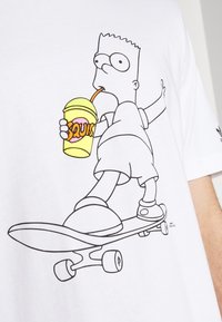 Vit bomull t-shirt med en tecknad figur på en skateboard som håller en gul dryck med ett sugrör. Enkel linjeteckning design.