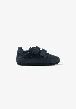 Zapatillas de piel negra con dos tiras de velcro, puntera redonda, paneles laterales texturizados y un emblema circular en el lado exterior.